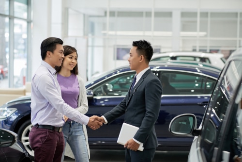 Young Asian salesman greeting a couple at a car dealership