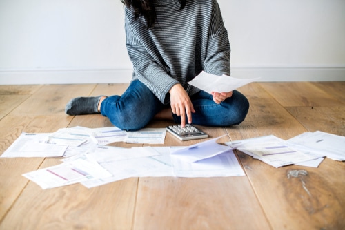A woman sitting on the floor with a calculator and sheets of financial papers. She may be worrying about her loan rejection.