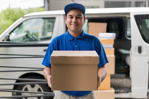 Young Asian man who is working as a delivery man is holding up a box to hand to the recipient of the package. Courier services is one of the unique business ideas listed in this article.