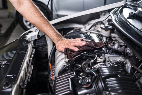 A mechanic uses a rag to polish the mechanism of a car beneath its open hood.