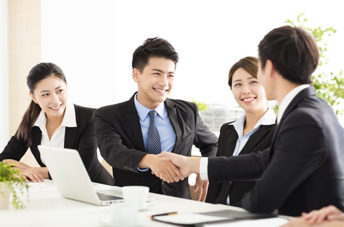 A group of 4 young Asian business people are smilling. Two of them are shaking hands. This ties into the article's discussion of how to register in PhilGEPS.