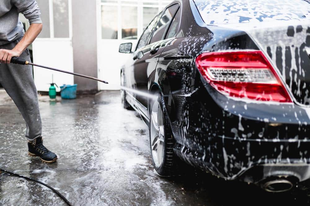 Image of a black car being washed with a hose. This relates to the concept of how to save money on car repairs.