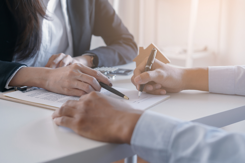 Two business people appear to be working on a contract. Both are holding pens, and one appears to be about to sign the contract. This is related to the topic of types of loan collateral.