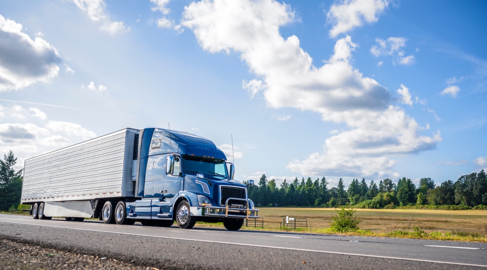 A blue ten-wheeler truck driving on a road. The blue sky is in the background. This image is relevant to the blog topic of "Buying a Truck? 10 Specifications You Need to Know".